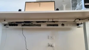 Under-desk cable management setup showing adhesive clips routing cords along the desk edge, a velcroed power strip, and a fabric cable sleeve, keeping the area tidy on a budget