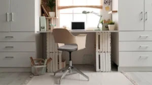 A converted closet home office (cloffice) with a wooden shelf desk, two floating shelves holding books and a small plant, LED strip lighting, and a curtain tied back on a tension rod