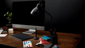 A dark academia desk decor setup with stacked leather-bound books, a brass lamp, a leather journal, and broad green accents on a walnut desk