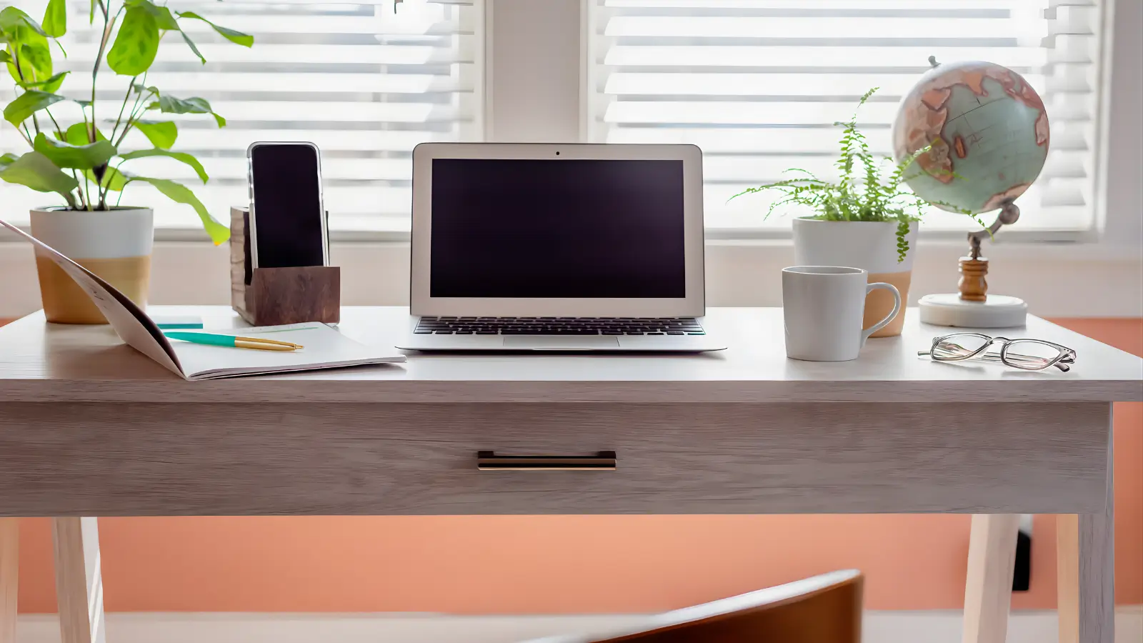 Home Office Desks for Women - A feminine home office with a woman’s desk, ergonomic chair, laptop, plant, and shelves in a bright, softly decorated room.