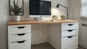 An IKEA countertop desk hack with a light wood surface resting on two white ALEX drawer units, styled with a monitor, small plant, and desk lamp in a bright room