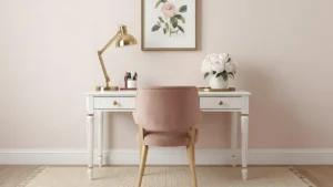 Soft romantic feminine home office with blush velvet chair, white desk, gold lamp, floral art print, and fresh peonies in a bright room