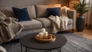 A cozy winter living room with navy and cream layered throws, a faux fur blanket, candle clusters on a wooden tray, and warm ambient lighting.