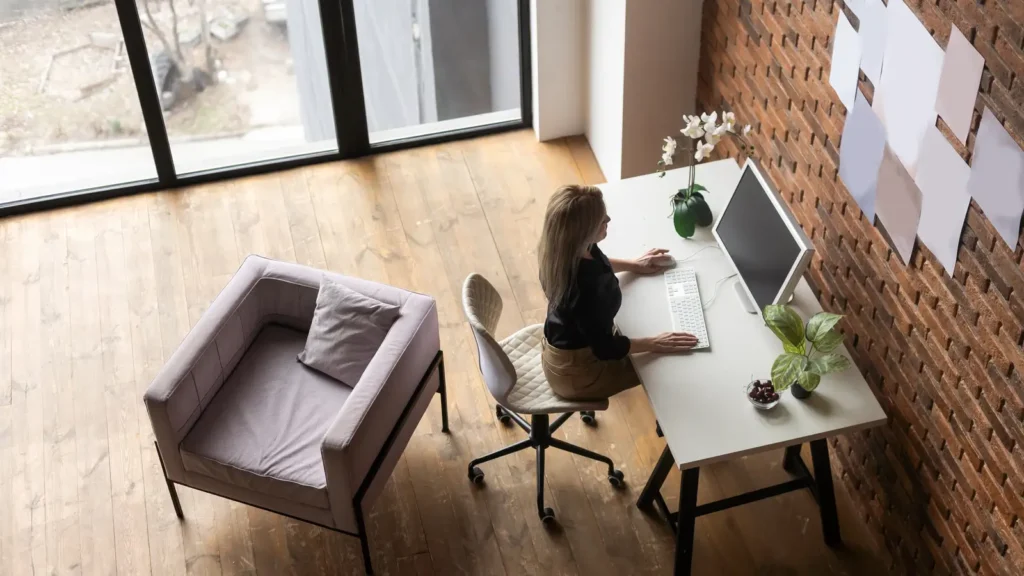 Ergonomic Chair Petite Women - A petite woman adjusting an ergonomic office chair in a bright home office with a desk, laptop, and soft neutral decor.